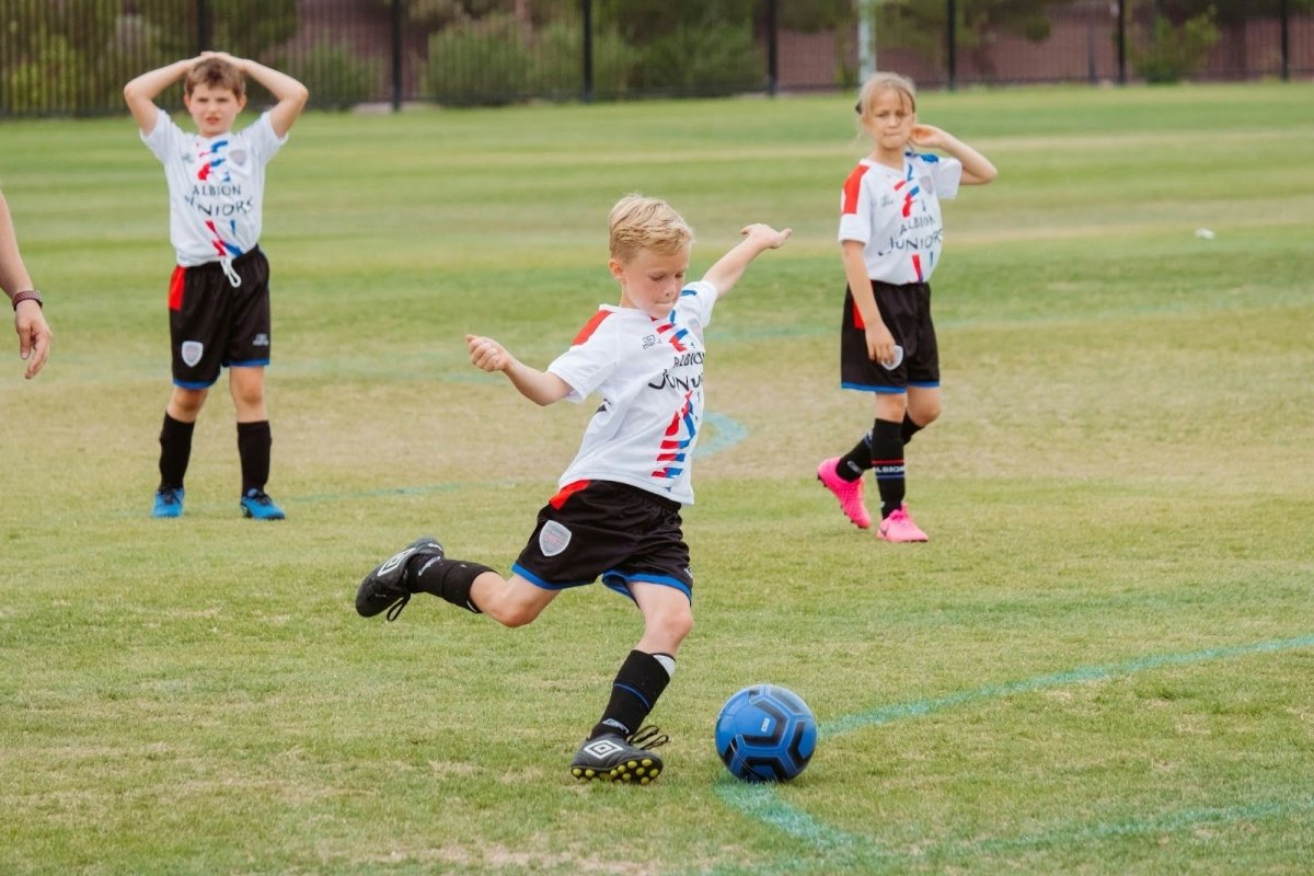 A boy kicking a soccer ball the right size for his age on the field.