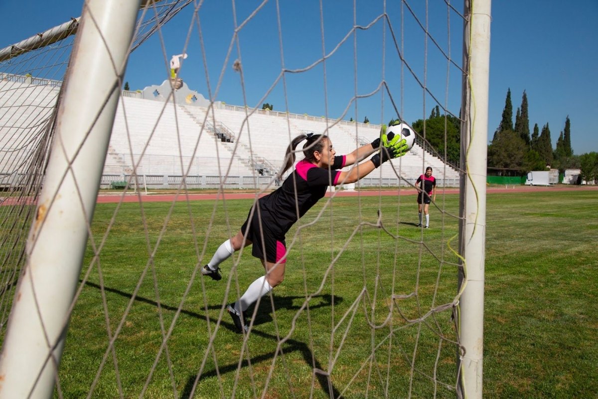Goalkeeper catching the ball in front of a properly sized soccer goal during practice.